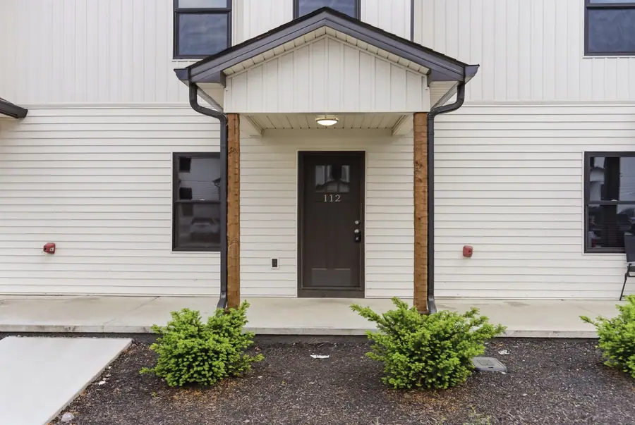 Front entry of a townhome unit under a covered porch, with low shrubs in the bed in front