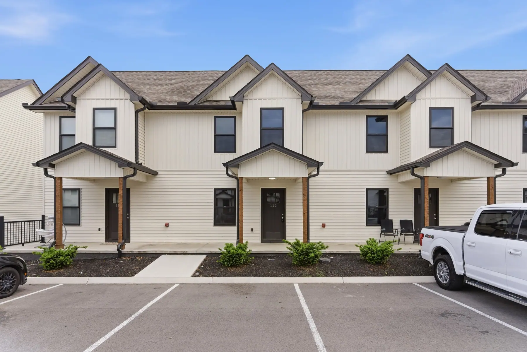 A row of two-storey townhomes with covered porch entries and the parking lot in front
