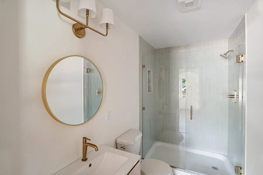 Bathroom with a glass shower, round mirror and brass fixtures