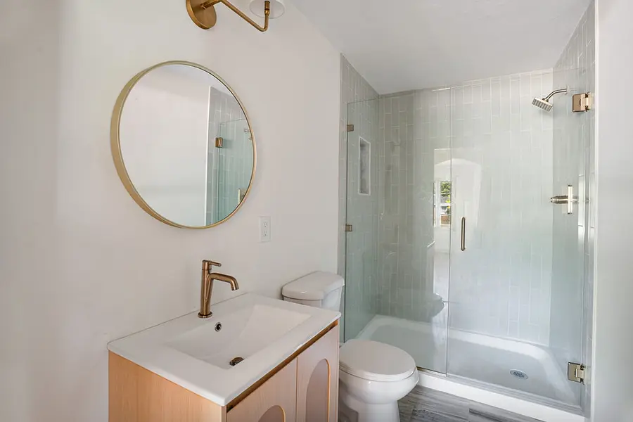 Bathroom vanity with a round mirror beside a glass shower